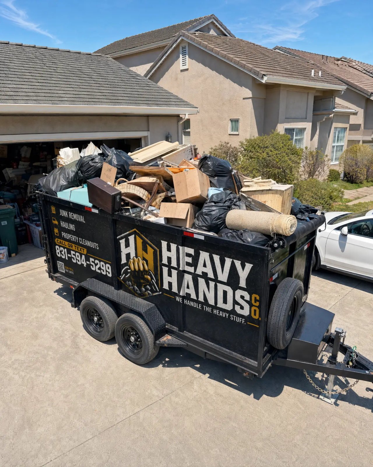 Loaded Heavy Hands Co. dump trailer in a Soledad driveway beside a garage being cleared out